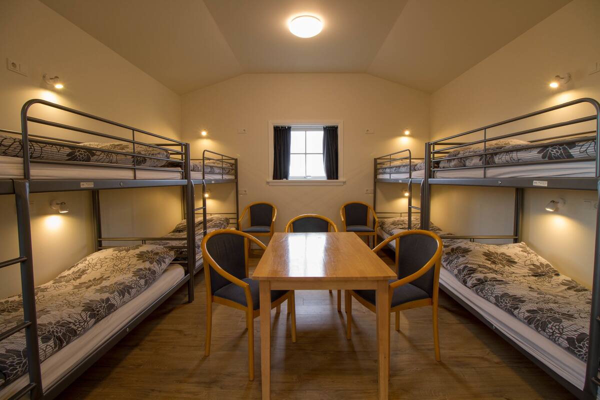 Une chambre de dortoir avec des lits superposés, une grande table en bois au centre et quatre chaises.
