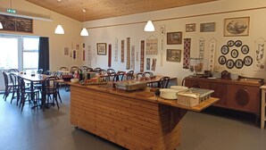 Een eetgedeelte met houten tafels en stoelen, een centraal bedieningspunt en diverse wanddecoraties.