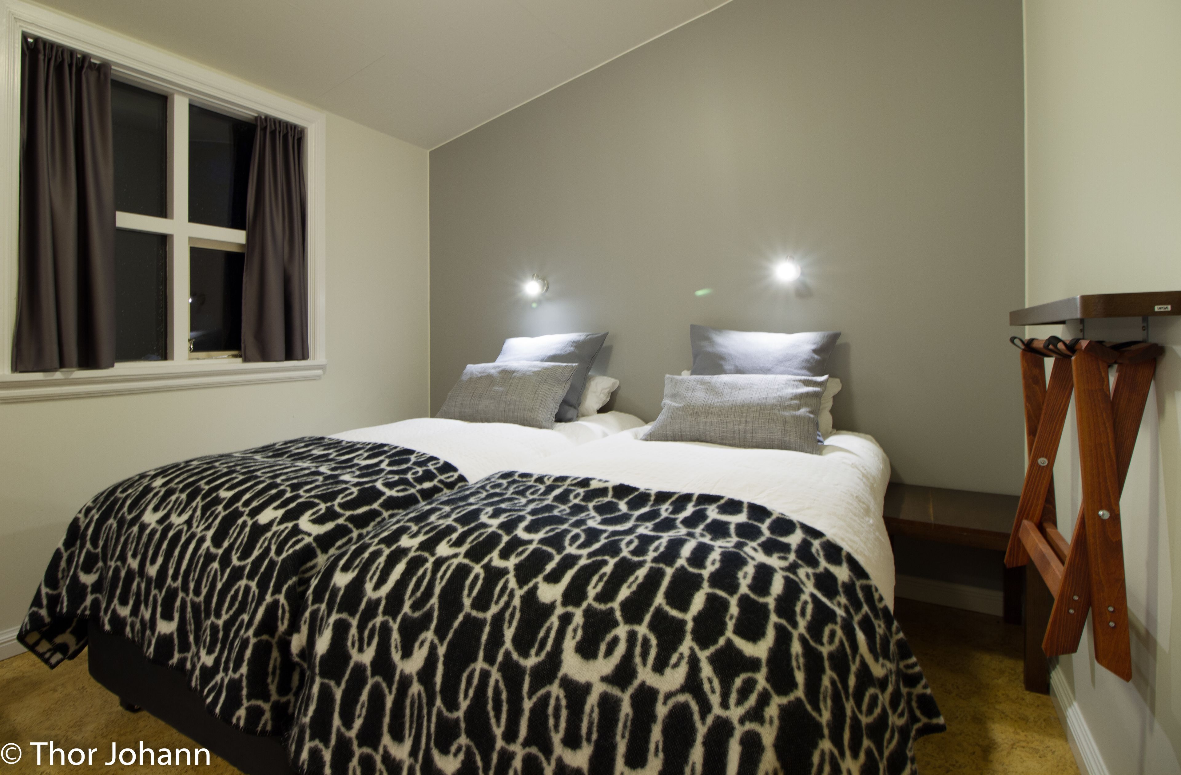 Un dormitorio con cama, dos mesitas de noche, una ventana con cortinas y un banco de madera.