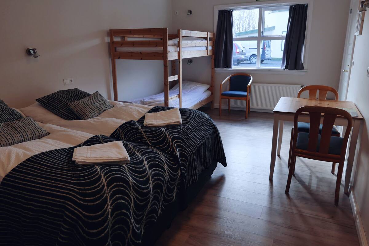 Une chambre de dortoir avec des lits superposés, une chaise, une table et une fenêtre donnant sur les voitures garées à l’extérieur.