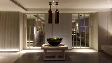 Un interior moderno con una mesa central que sostiene un cuenco decorativo, flanqueada por persianas verticales y una zona de estar.
