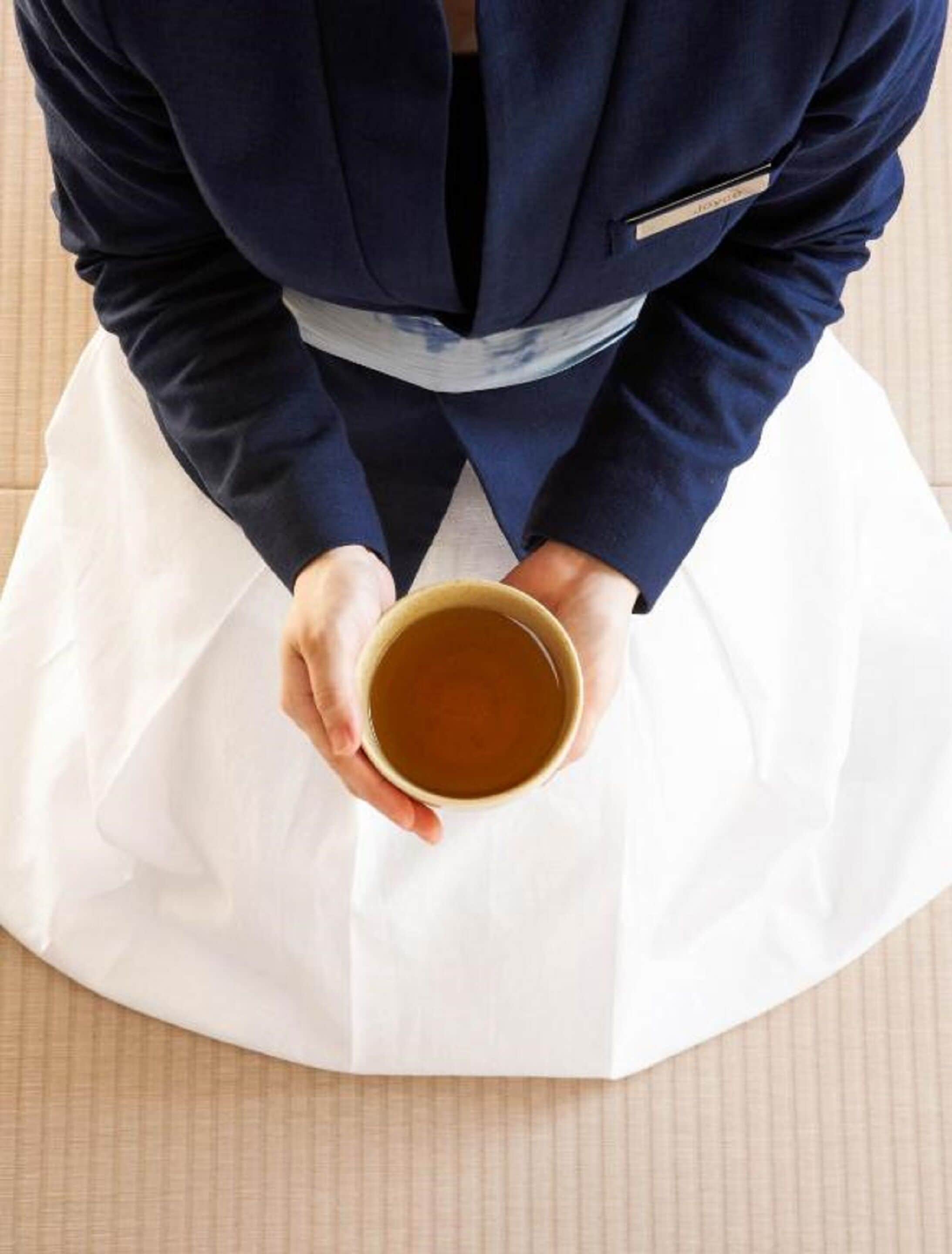A person seated on a tatami mat holding a cup.