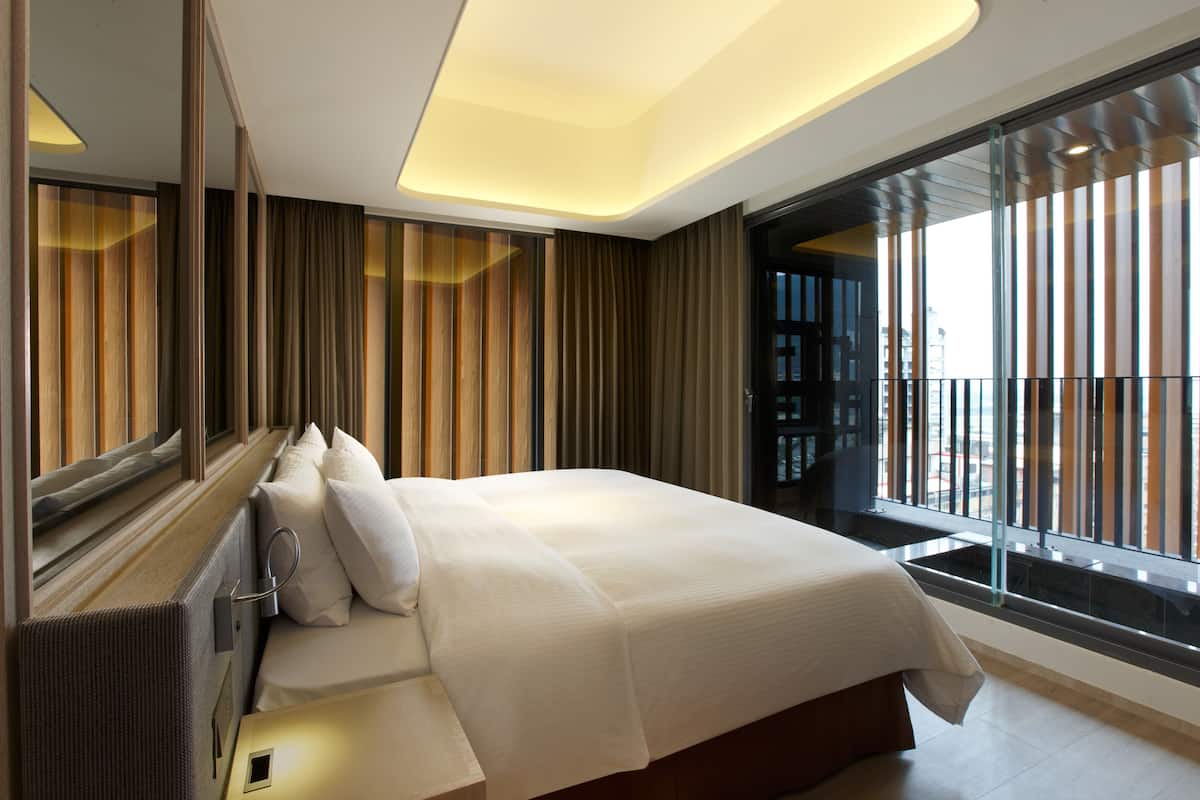 Ett modernt hotellrum med en stor säng, utsikt genom en glasvägg och en samtida design.