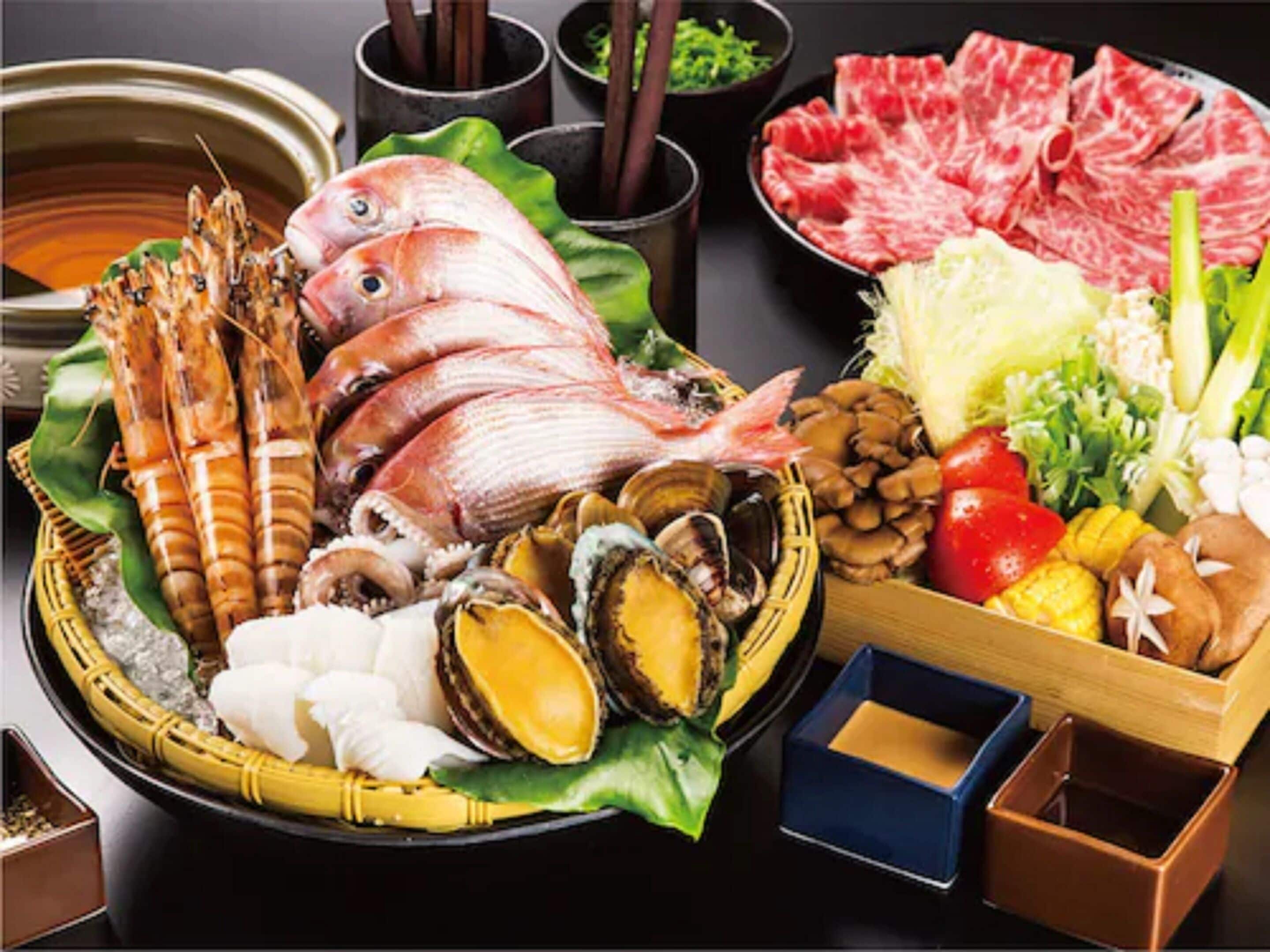 A variety of seafood and meat dishes, including shrimp, fish, clams, and beef, arranged on a table with bowls of dipping sauces.