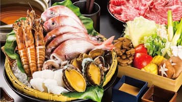 A variety of seafood and meat dishes, including shrimp, fish, clams, and beef, arranged on a table with bowls of dipping sauces.