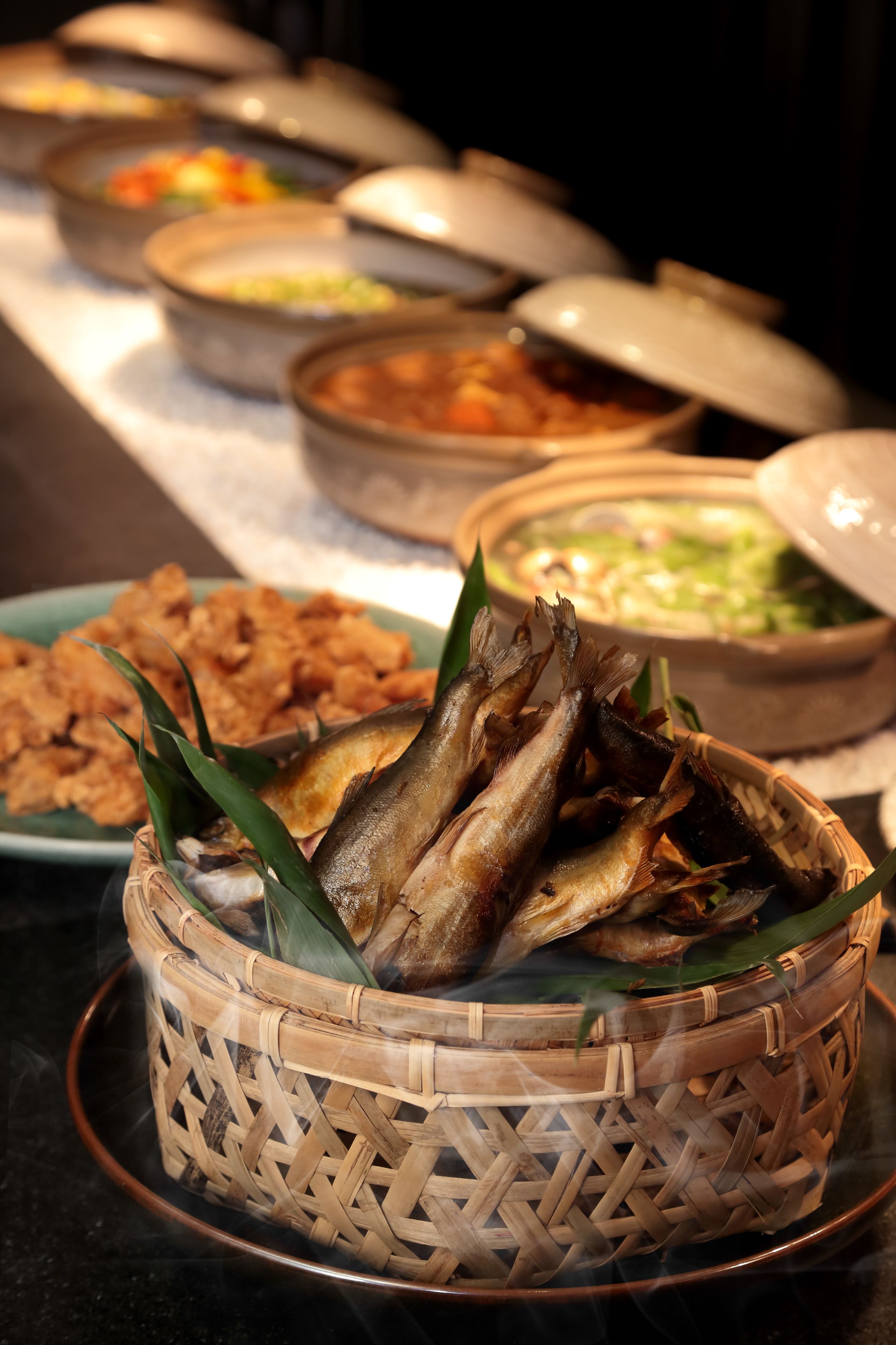 A buffet table with various dishes, including a basket of fried fish and several bowls of different foods.
