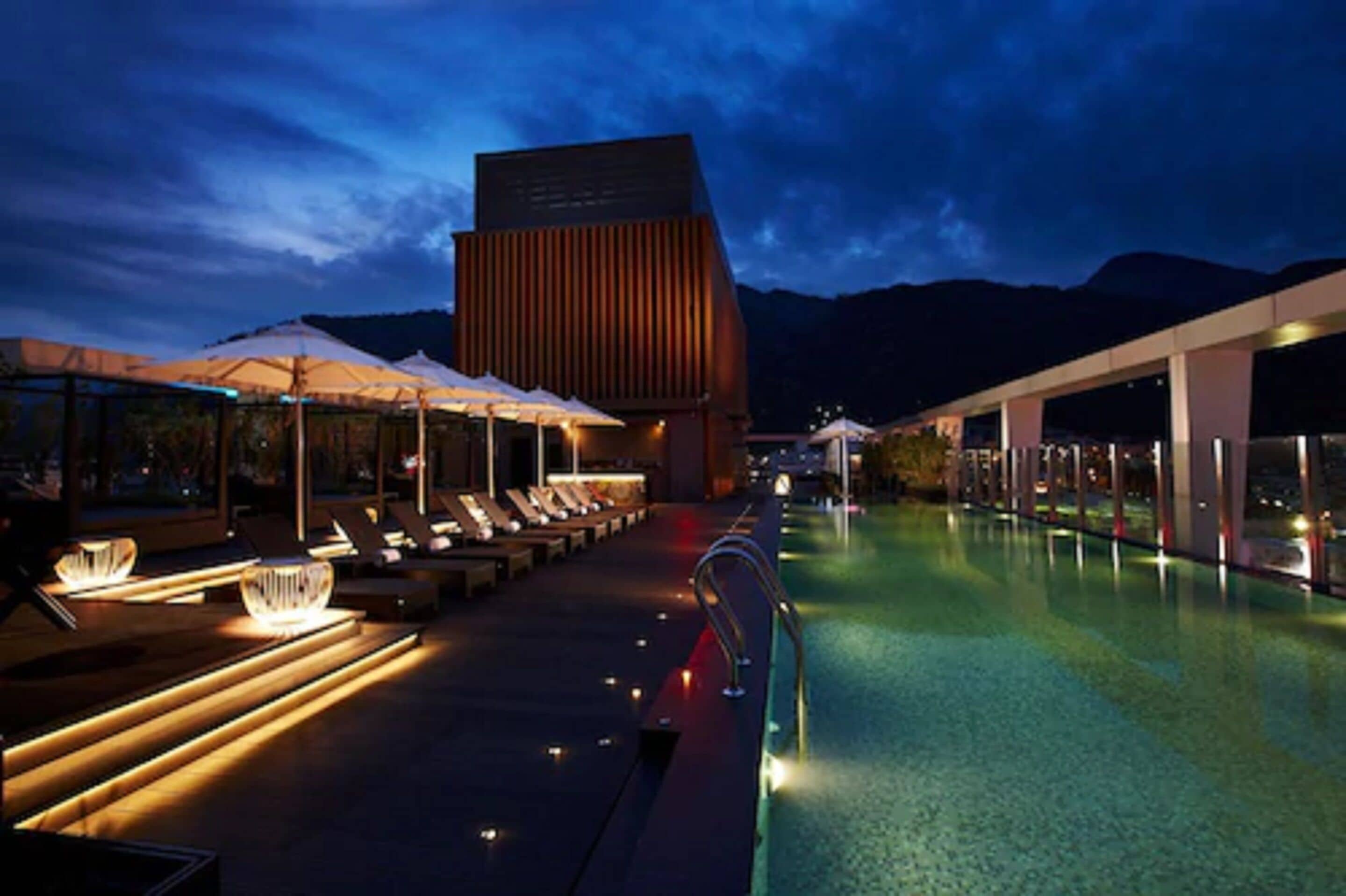 A poolside area with lounge chairs and umbrellas, a modern building, and a clear sky.