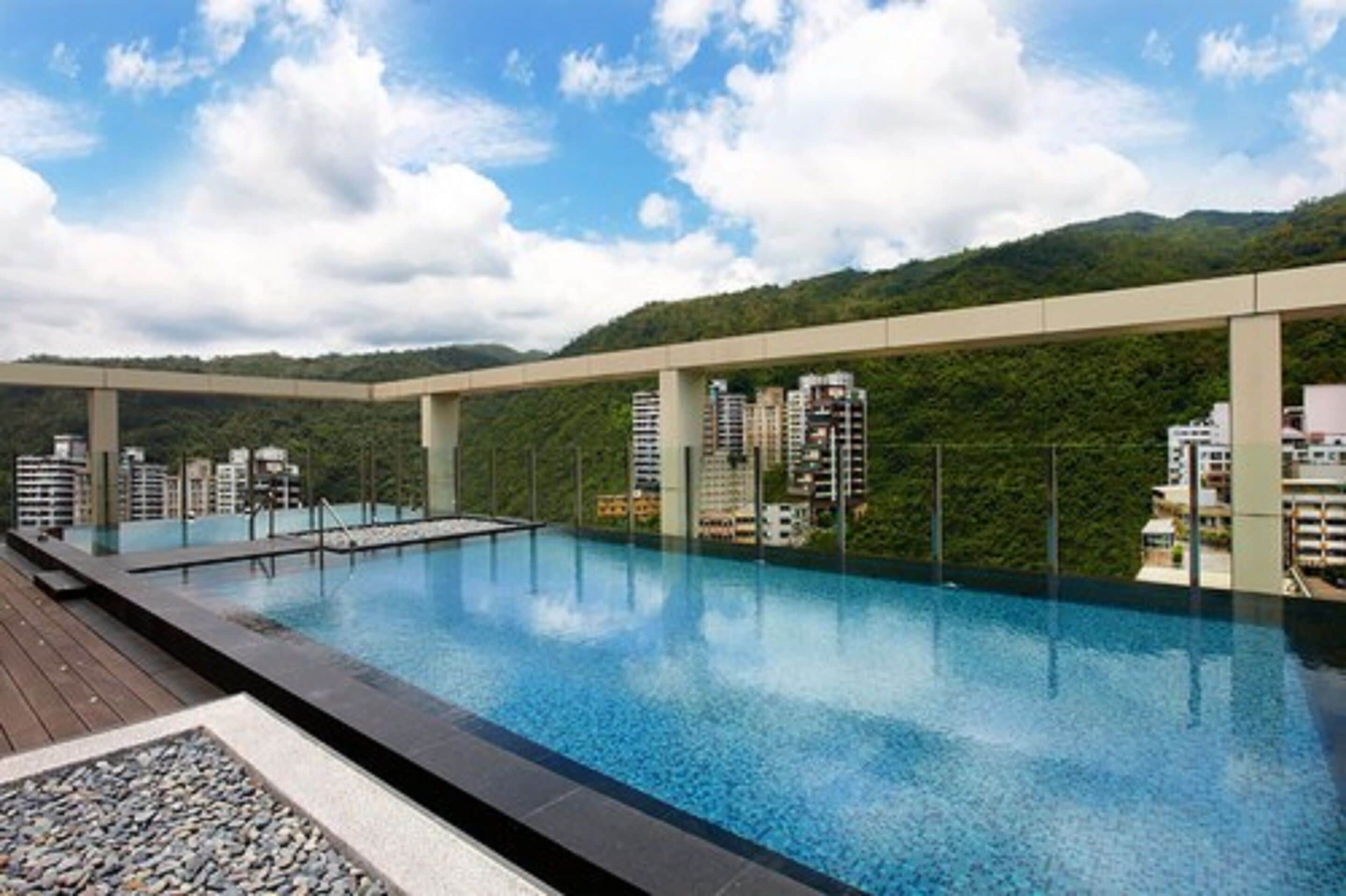A rooftop infinity pool with a view of a cityscape and mountains.