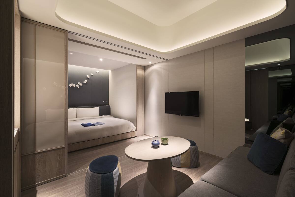 Ett modernt hotellrum med en säng, ett runt bord med en vattenkokare och en tv som är monterad på väggen.