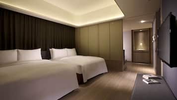 A modern hotel room with two beds, a flat-screen TV, and a small seating area.