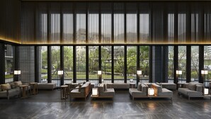 Een moderne lobby met grote ramen, meerdere zithoeken en vloerlampen.