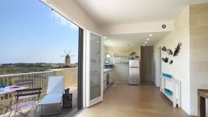 Un balcón con mesa y sillas, una cocina con refrigerador y armarios, y un molino de viento al fondo.