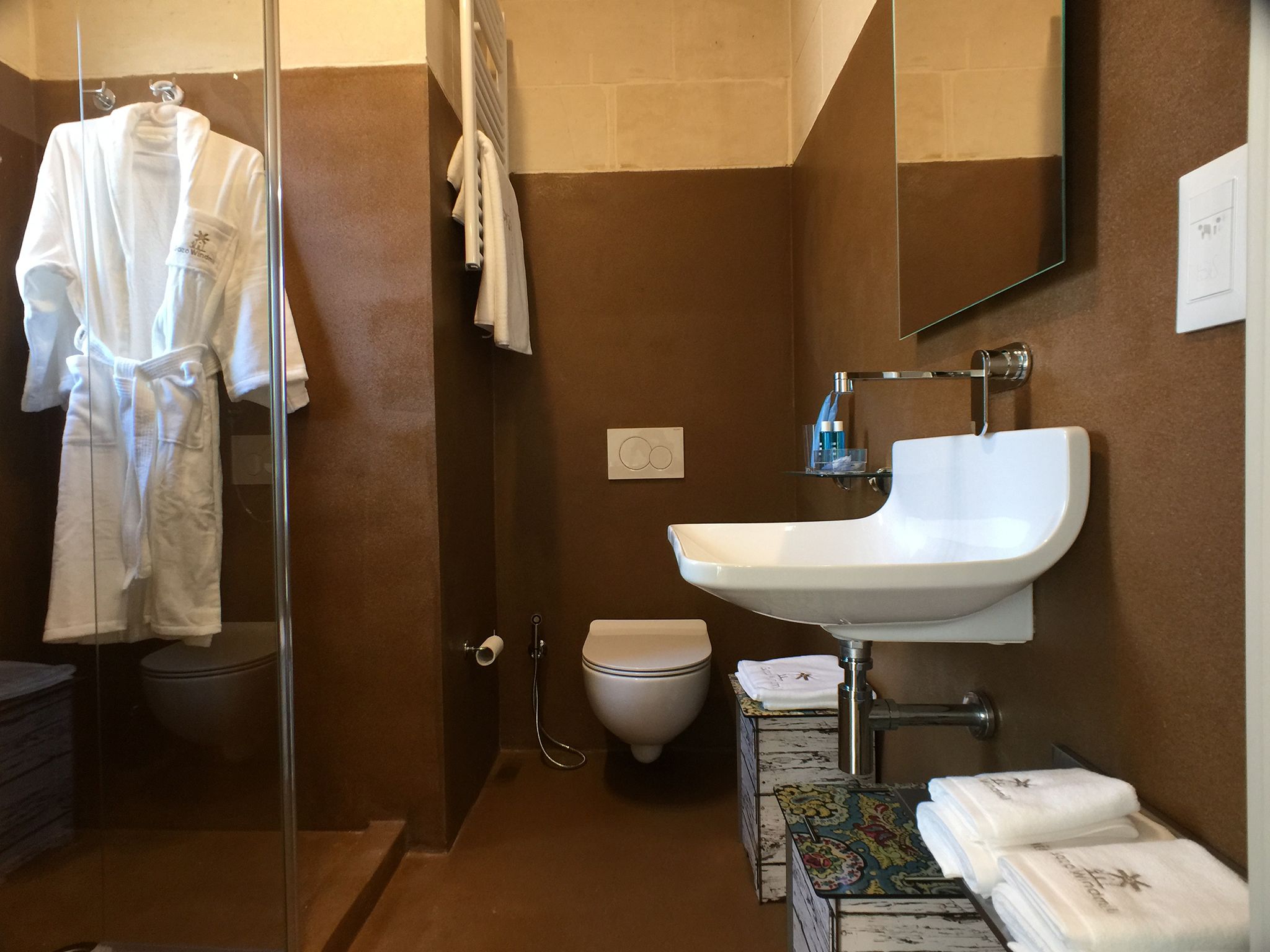 Un baño con cabina de ducha de vidrio, un lavabo blanco, un inodoro y una mesita con toallas.