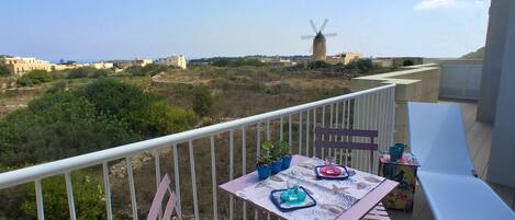 A balcony with a table set for two, overlooking a landscape with a windmill in the distance.