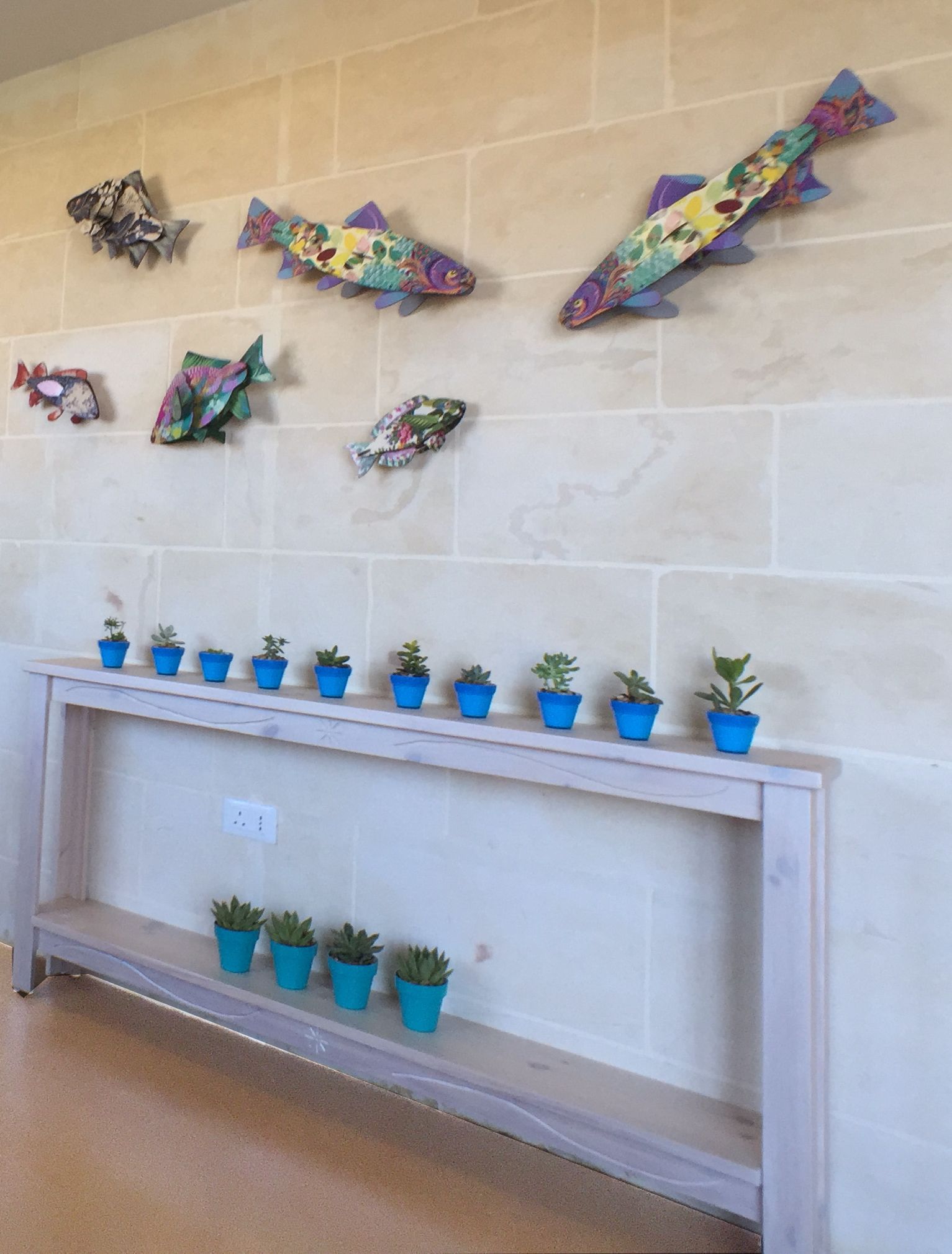 A wall with decorative fish and a shelf with potted plants.