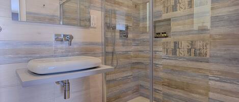 A modern bathroom with a glass shower enclosure, a white sink, and a mirror above it.
