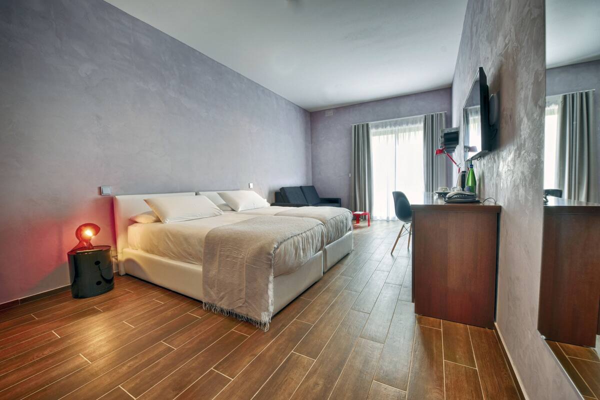 A modern hotel room with a large bed, a desk, and a TV mounted on the wall.