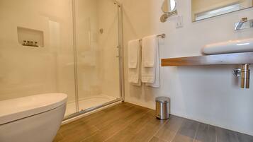A modern bathroom with a glass shower enclosure, a toilet, a sink with a mirror, and a trash can.