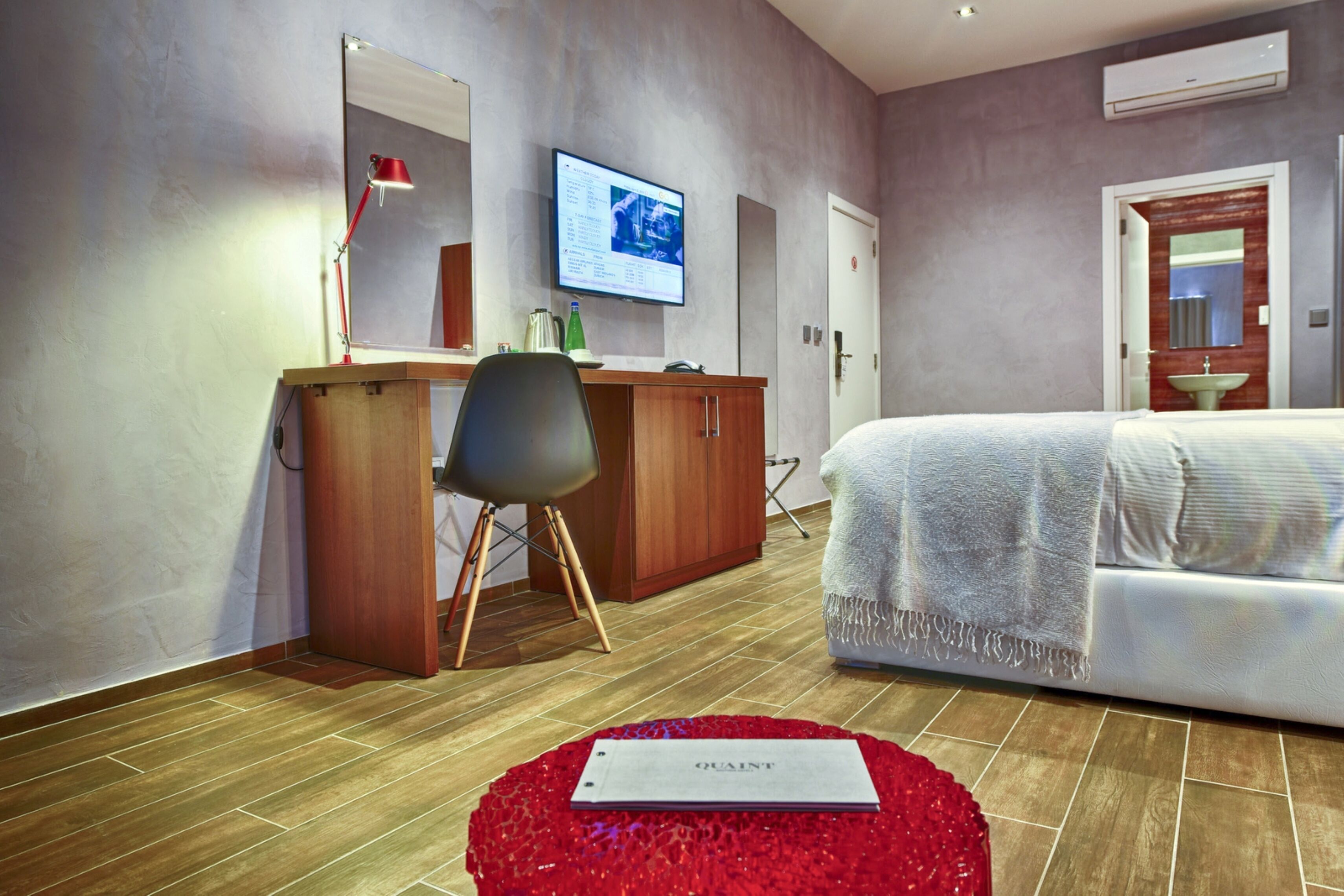 Ein modernes Hotelzimmer mit einem Holztisch, einem großen Bett, einem an der Wand befestigten Fernseher und einem roten Teppich.