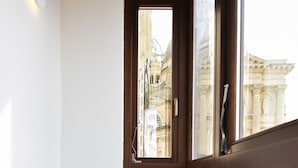 Un pasillo estrecho con una puerta y ventana de madera, una mesa redonda de madera, y vista a un edificio clásico en el exterior.