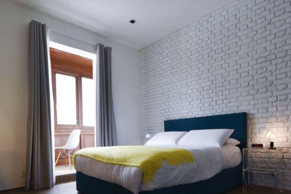 A modern bedroom with a large bed, a white brick-patterned wall, and a wooden floor.