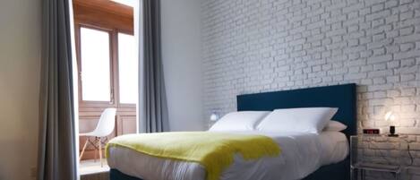 A modern bedroom with a large bed, a white brick-patterned wall, and a wooden floor.