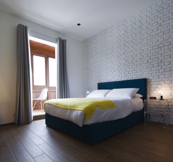 A modern bedroom with a large bed, a white brick-patterned wall, and a wooden floor.