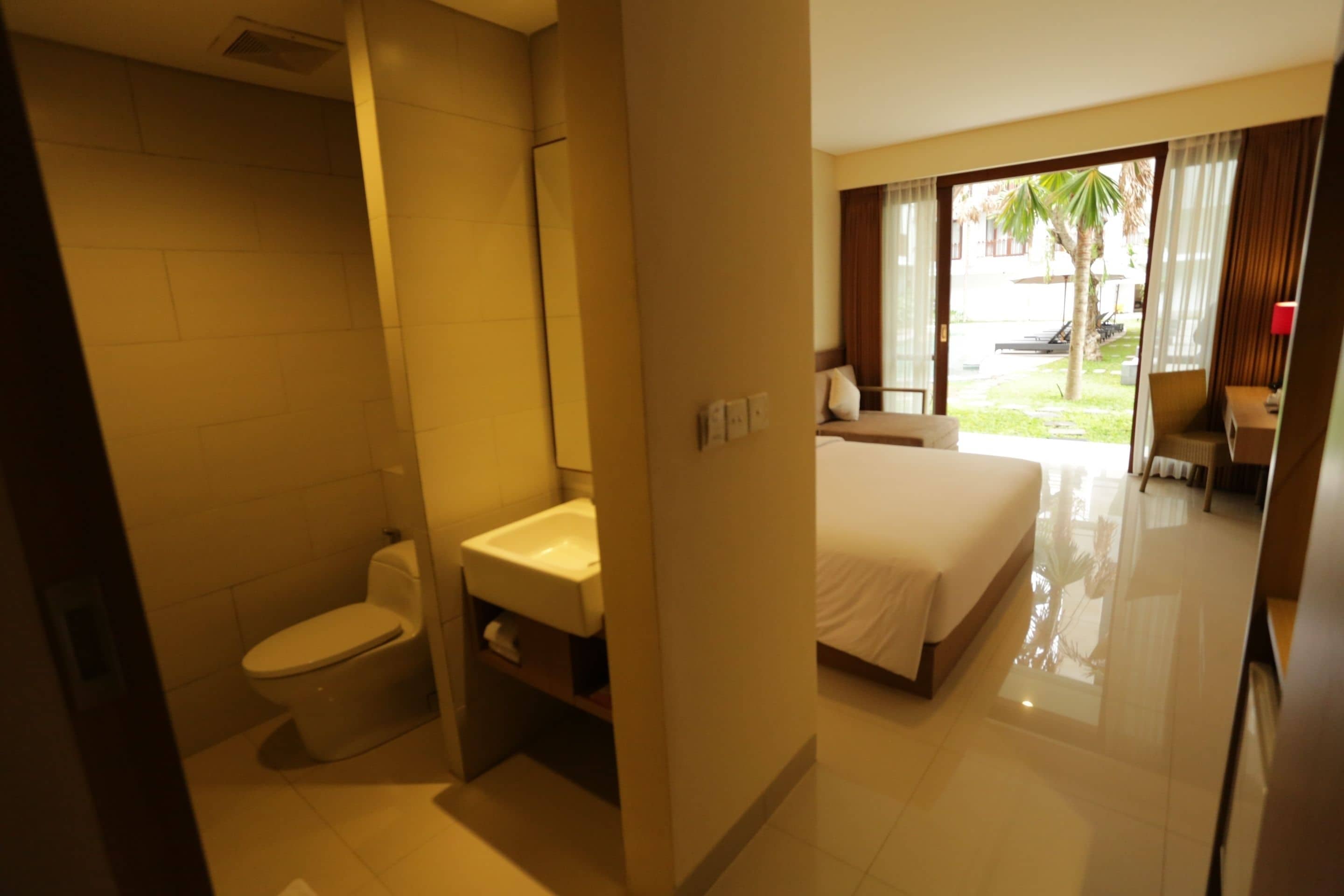 A hotel room with a bathroom, a bed, and a view of the outside.