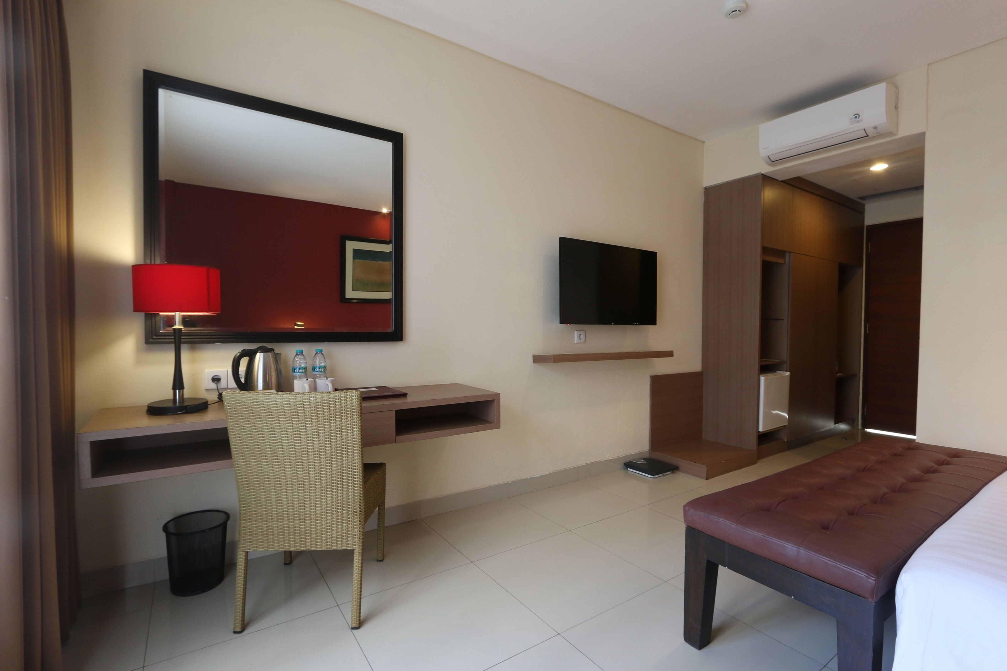 A hotel room with a bed, a desk with a chair, a television, and an air conditioning unit.