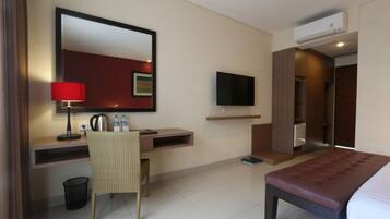 A hotel room with a bed, a desk with a chair, a television, and an air conditioning unit.