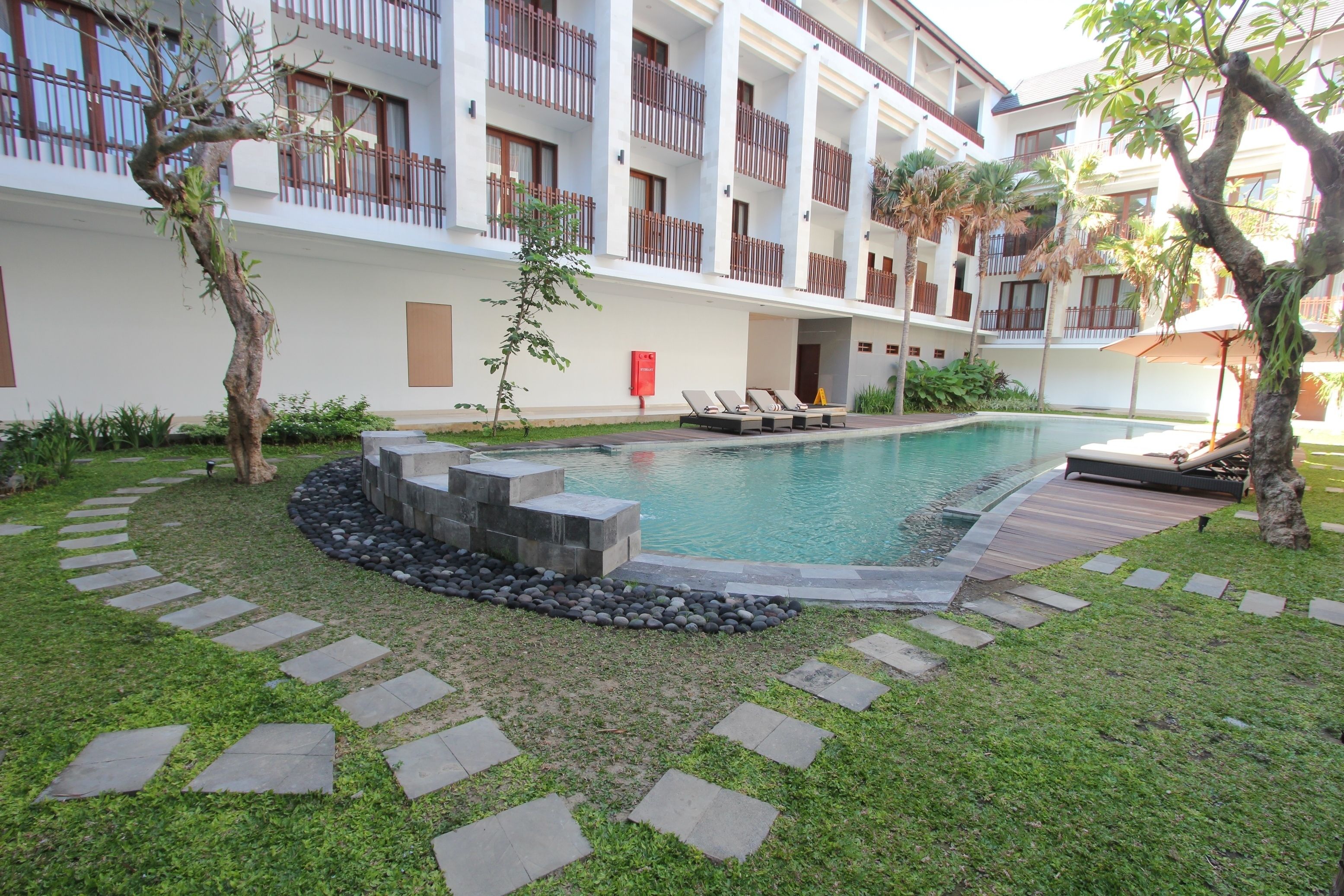 A pool area with lounge chairs, a stone pathway, and a building with balconies.