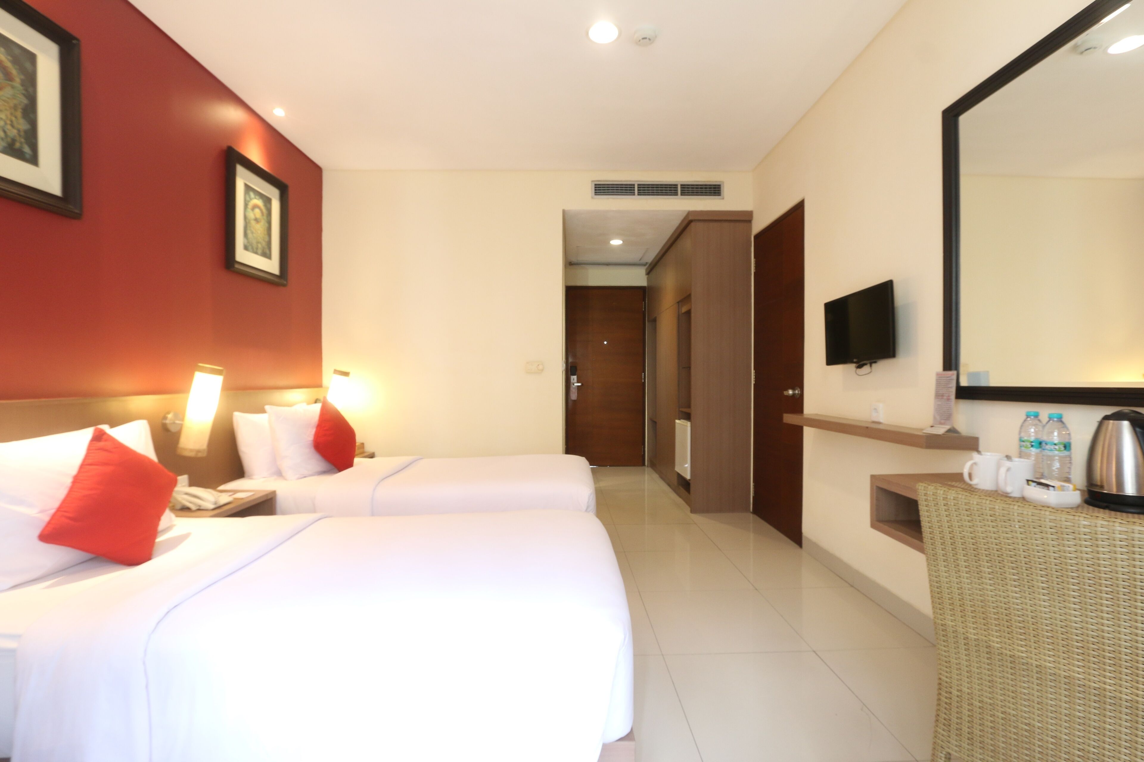 A hotel room with two beds, a television, a minibar, and a bathroom visible through an open door.