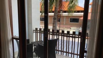 A balcony with wicker furniture and a view of a street with buildings and a palm tree.