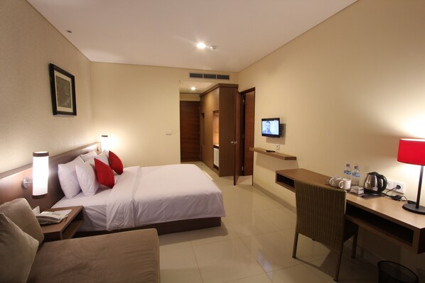 A hotel room with a bed, a desk, a chair, a TV, and a red lamp. - Grand La Walon Hotel (Kuta)