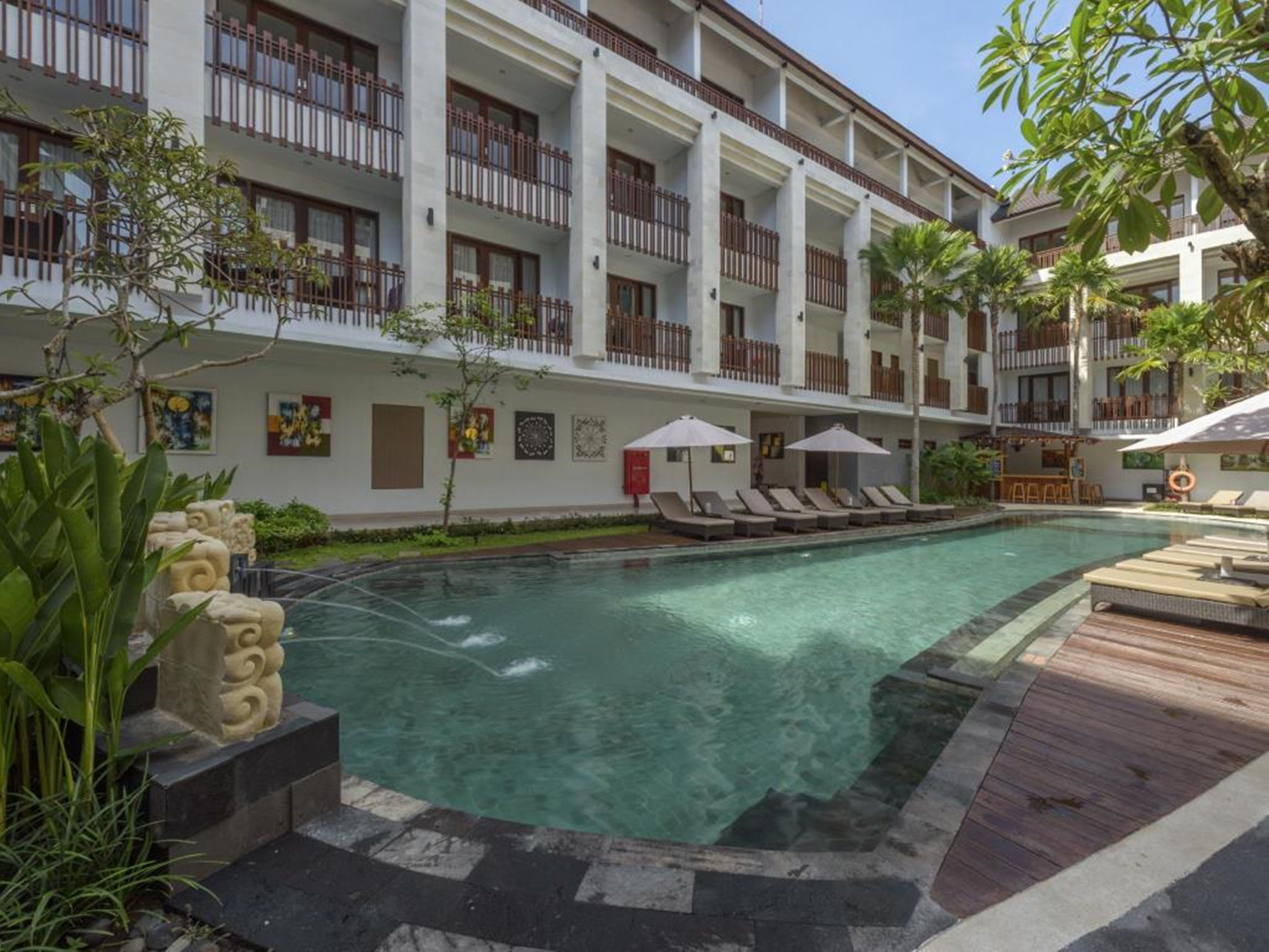 A hotel with a swimming pool, multiple balconies, and lounge chairs.