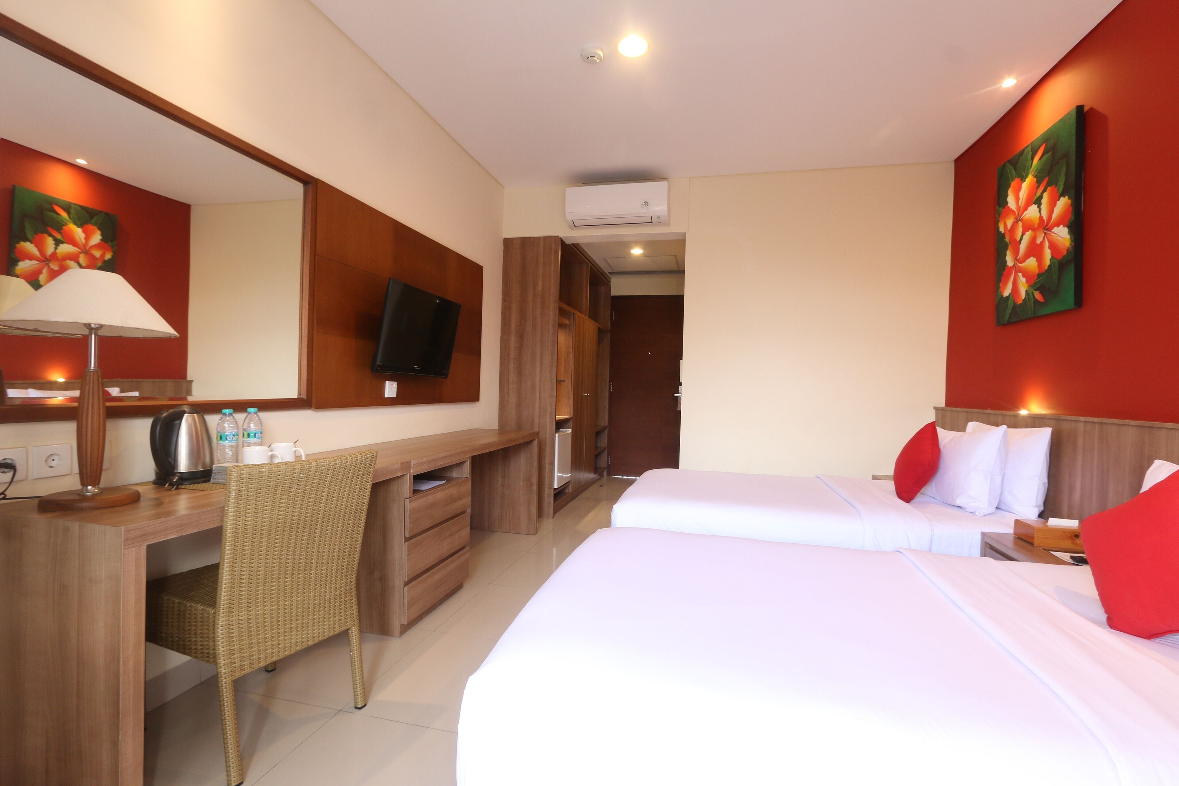 A hotel room with a desk, two beds, a television, and a red floral wall painting.