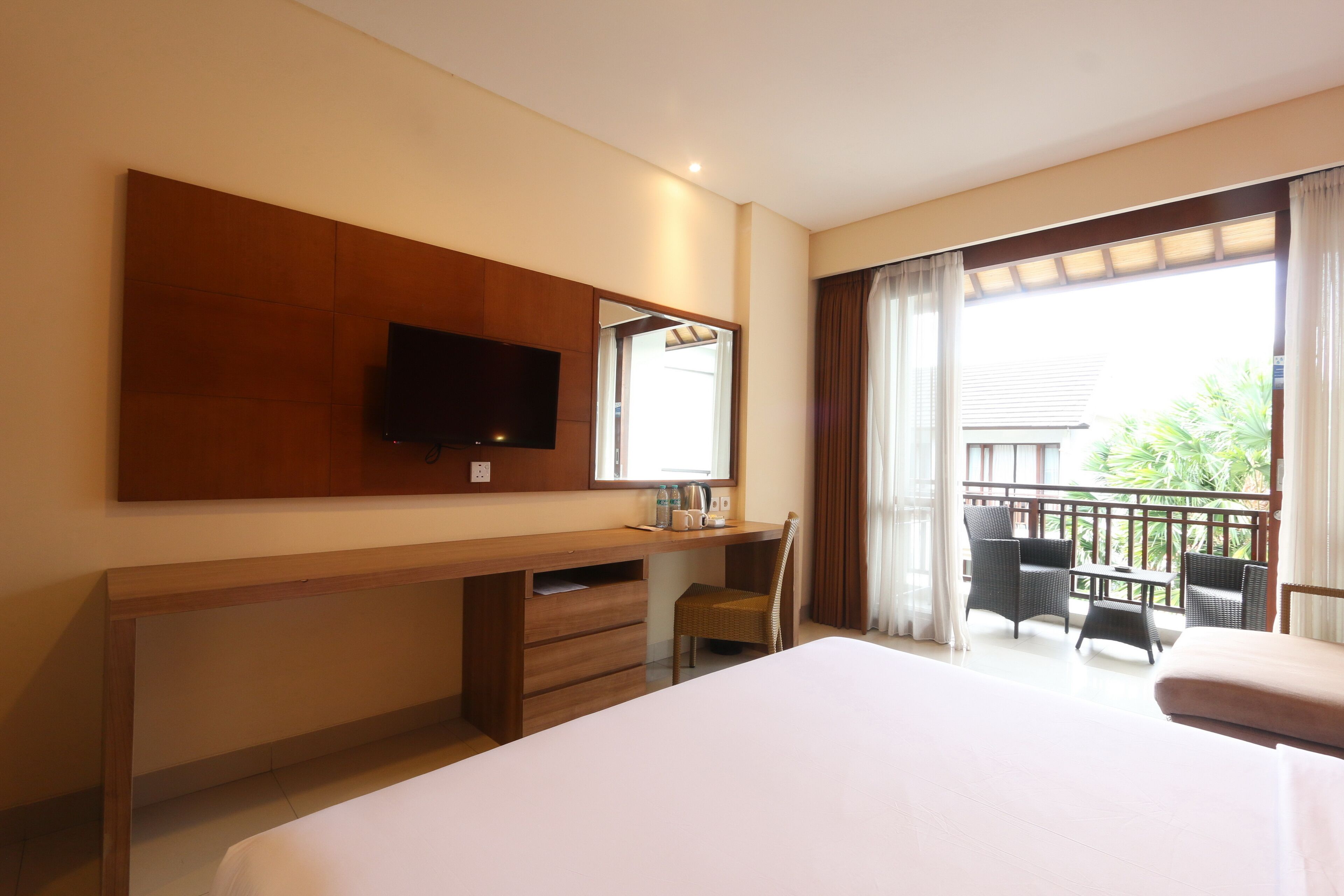 Ein Hotelzimmer mit Bett, Schreibtisch, Stuhl, Fernseher und einem Balkon mit Sitzgelegenheiten.