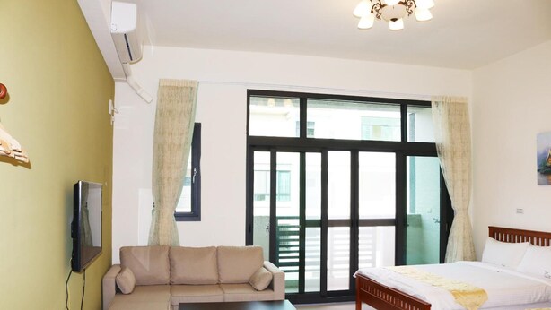 A hotel room with a sofa, a bed, a TV, and a sliding glass door to the outside. - Kenting MuChen INN (Hengchun)