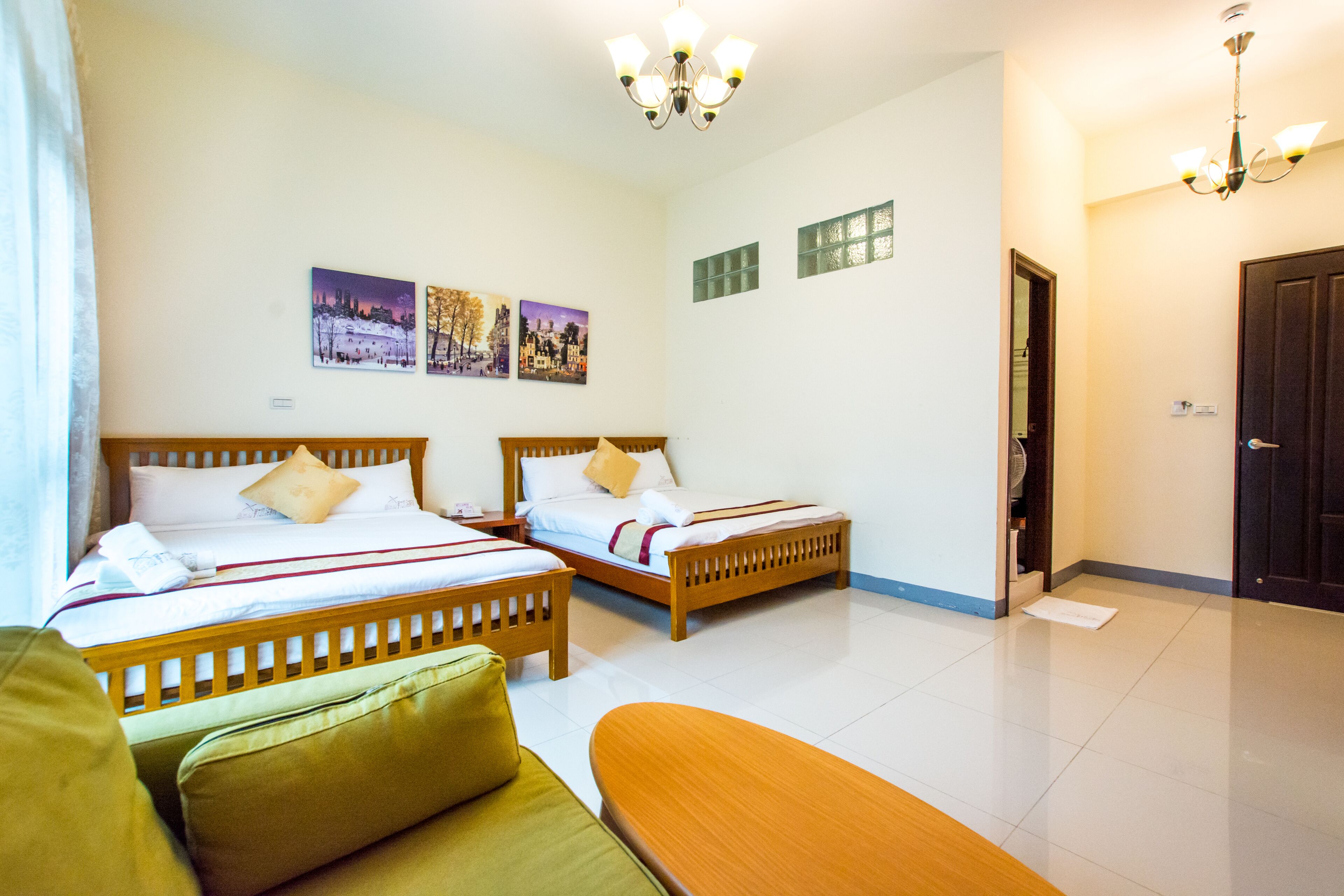 A hotel room with two wooden beds, a green sofa, a wooden bench, and a chandelier.
