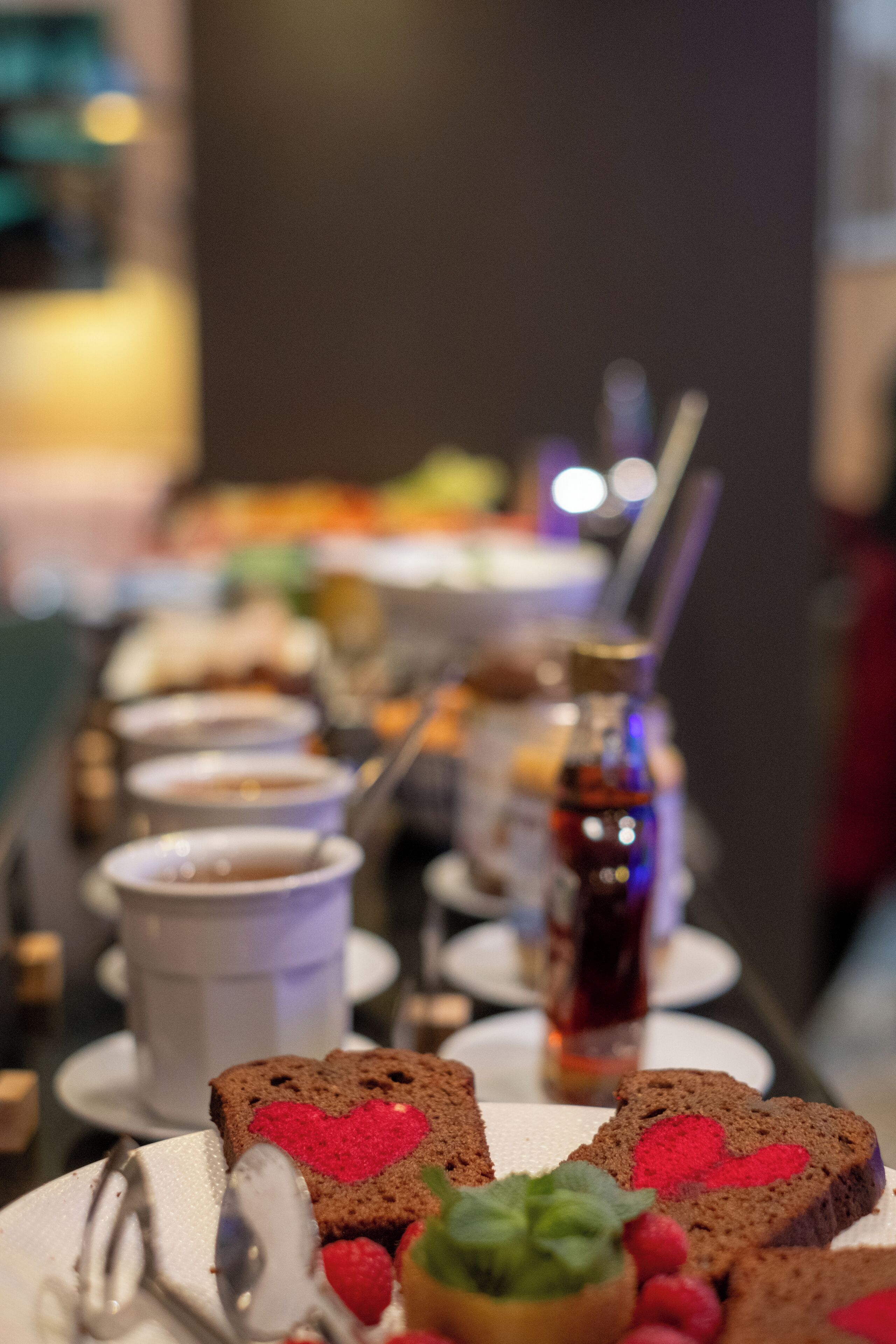 A table with various food items and drinks, including bread with heart-shaped decorations, a small bowl of fruit, and a bottle of syrup.
