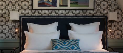 Un lit bien fait, avec des oreillers blancs et à motifs, un oreiller bleu à motifs et une tête de lit agrémentée de lampes fixées au mur.