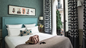 A hotel room with a teal headboard, a bed with white linens, a patterned throw, a framed picture above the bed, and a view of the outside balcony through sheer curtains. - Hôtel Adèle & Jules (Paris)