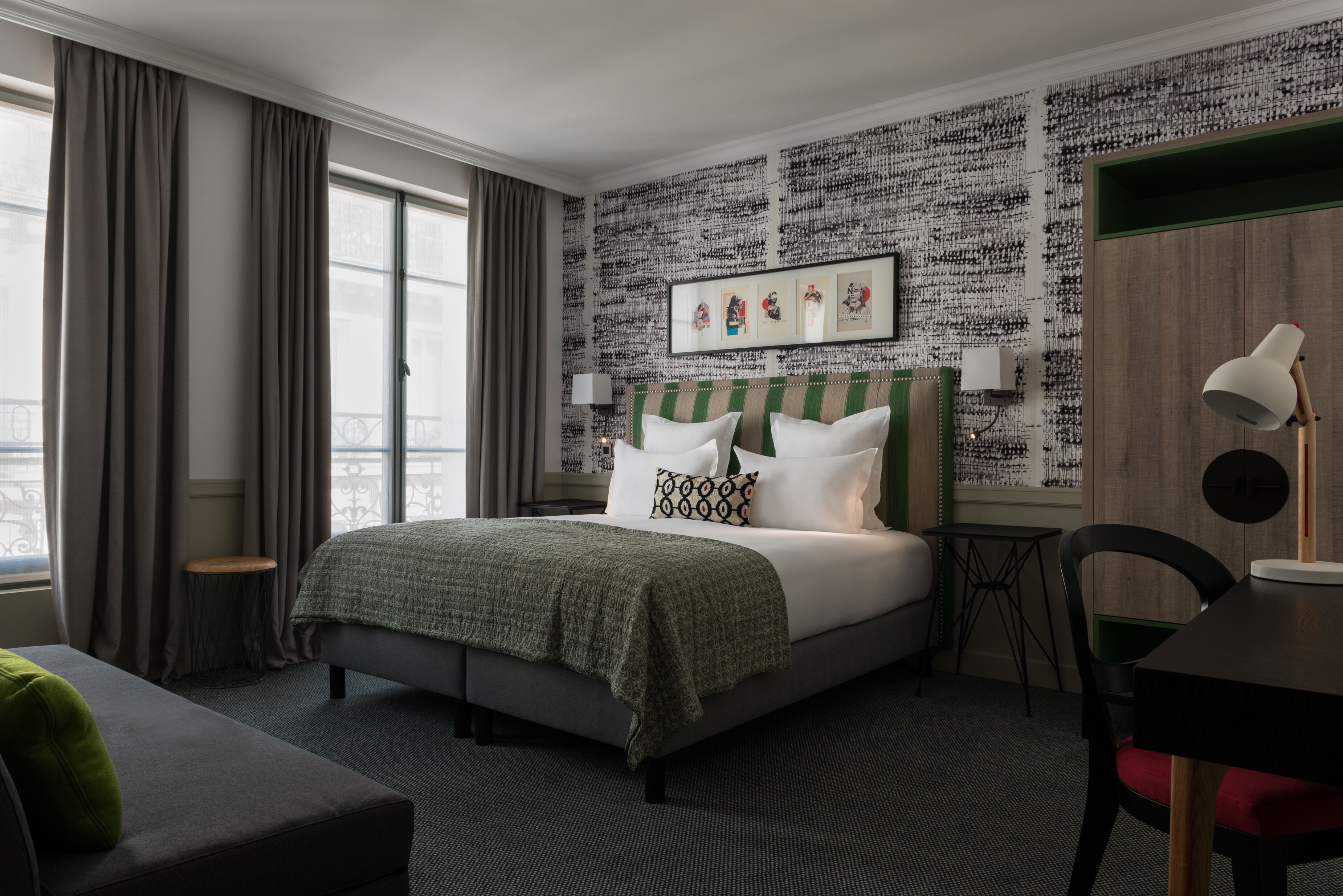 A hotel room with a large bed, a small table, a chair, and a window with curtains.