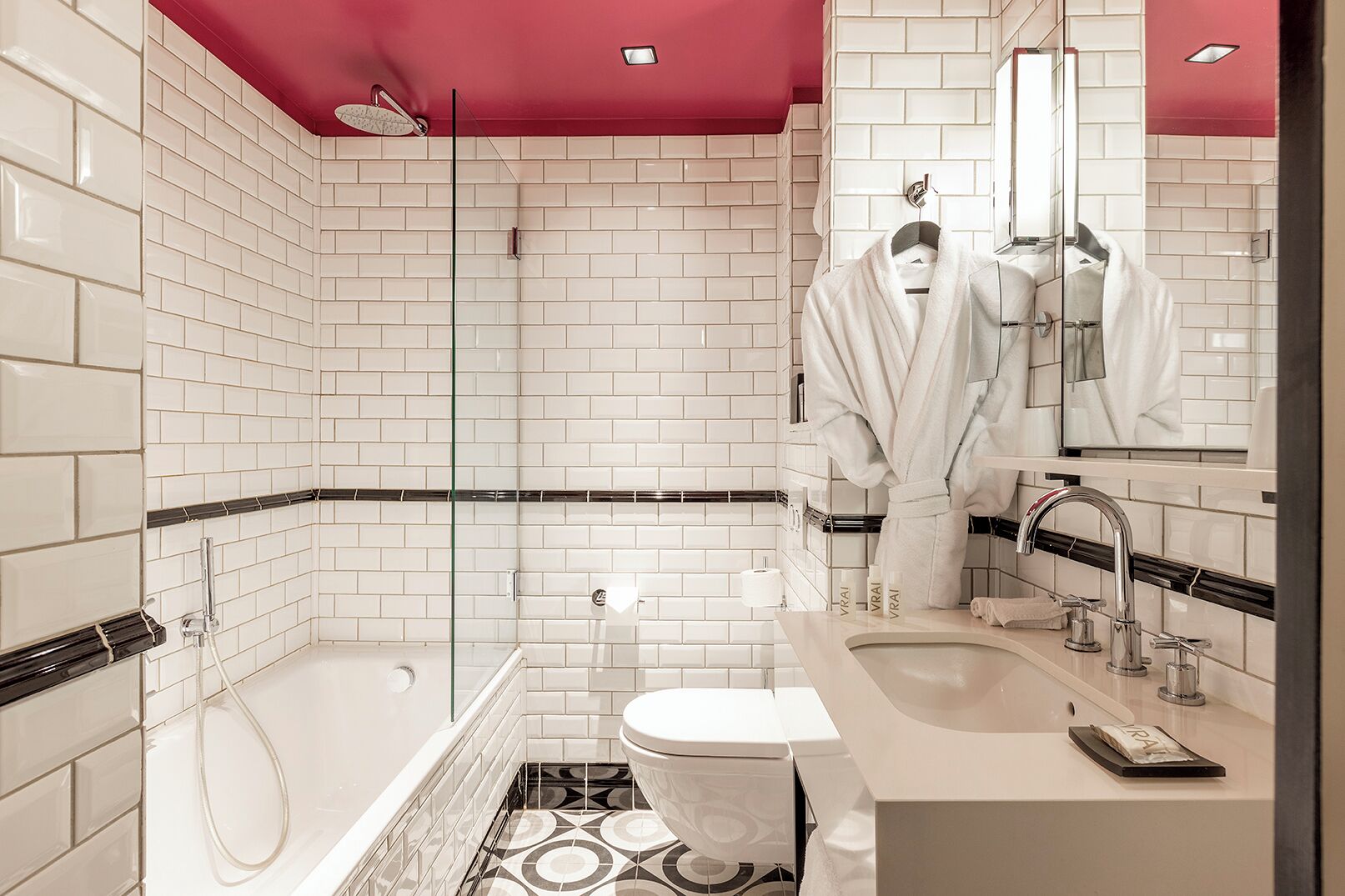 A modern bathroom with white subway tiles, a glass shower enclosure, a toilet, and a sink with a mirror.