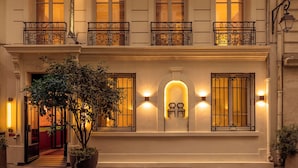 A hotel facade with ornate iron railings, a large potted plant, and illuminated wall sconces. - Hôtel Adèle & Jules (Paris)
