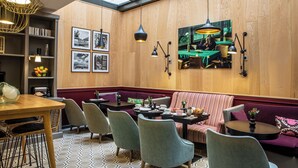 A cozy restaurant with wooden walls, a high ceiling, and a skylight. There are multiple tables and chairs, and a large window displaying a scene of people dining. - Hôtel Adèle & Jules (Paris)