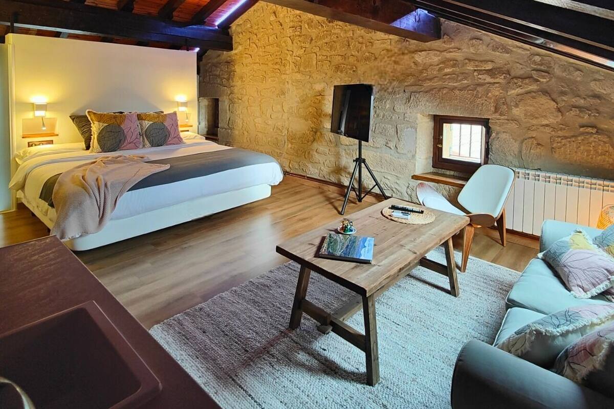 A cozy bedroom with a large bed, a wooden table, a chair, and a small window.
