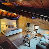 Quarto aconchegante com uma cama grande, uma mesa de madeira, uma cadeira e uma janela pequena.