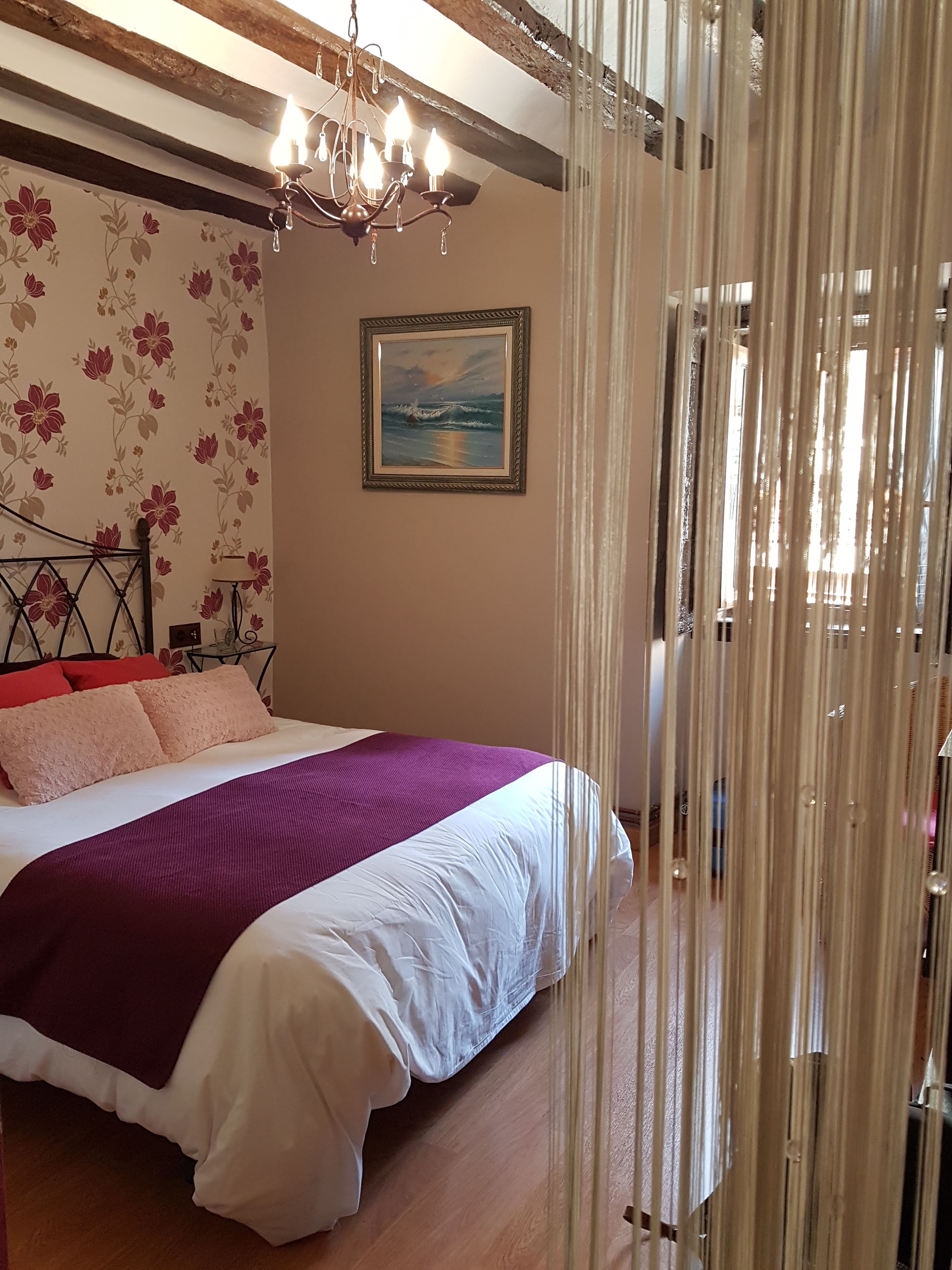A bedroom with a bed, a chandelier, a painting, and curtains.
