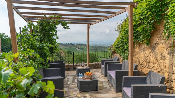 A covered outdoor seating area with wicker furniture and a stone floor, overlooking a scenic landscape. - Casa Rural La Molinera Etxea (Samaniego)